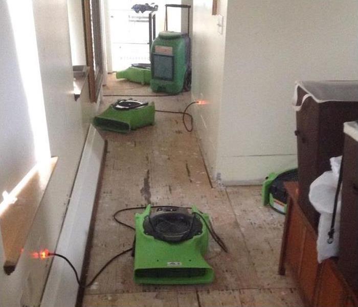 Room with hardwood floor removed and three air movers and a dehumidifier set up in the area.