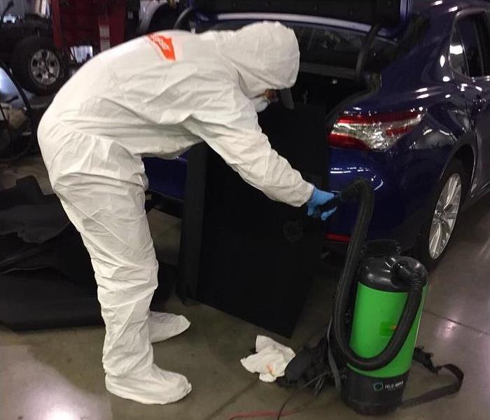 Man in white suit working in the trunk of a car.