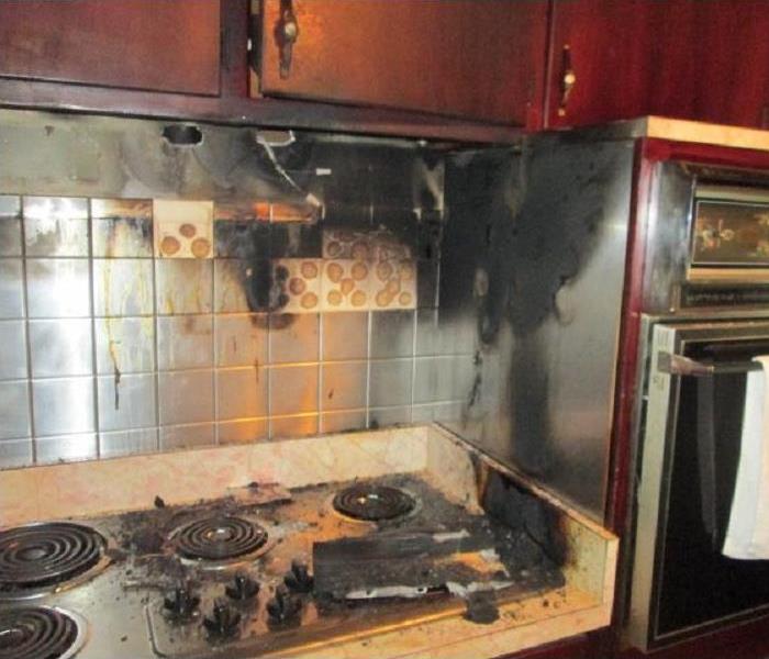 Kitchen stove with wood cabinets above that are all damaged by fire.