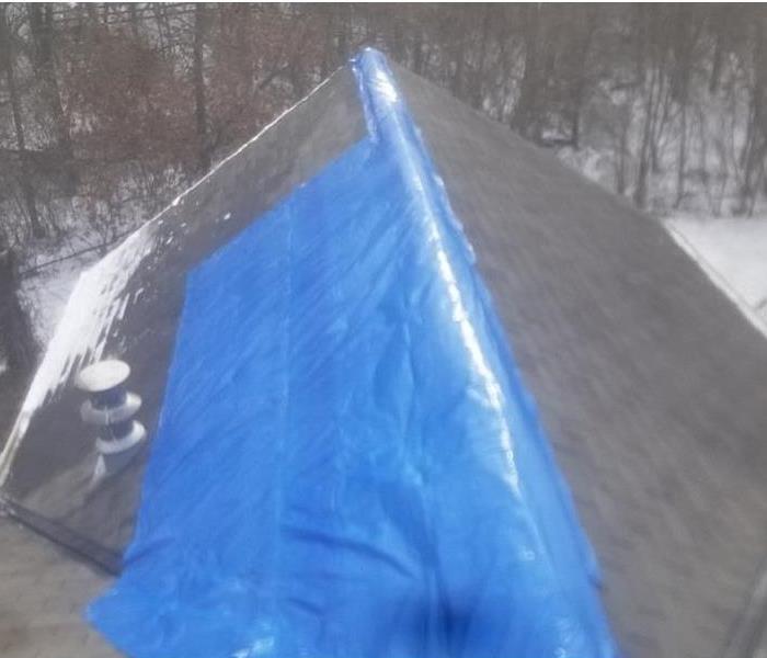 Roof of a home partially covered by a blue tarp.